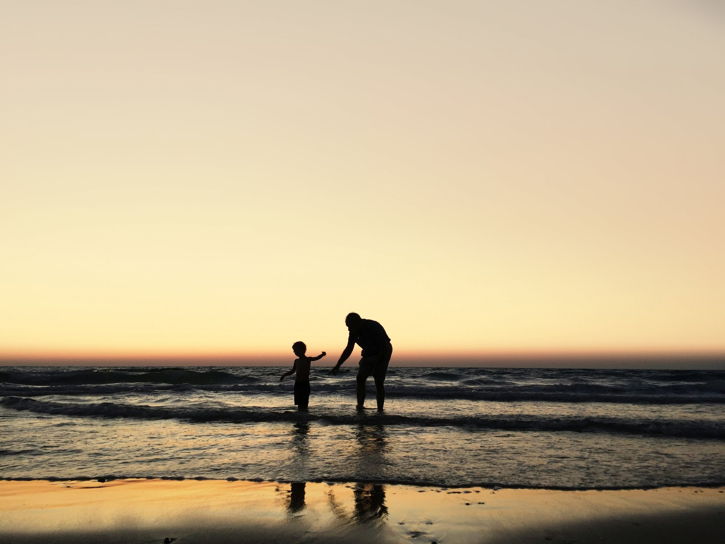 A grandfather and his grandson at the water's edge at sunset